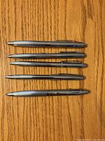 Five metal multi-colour pens arranged horizontally on wood surface