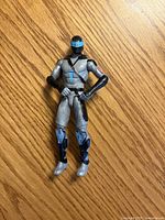 Front view of grey, black and blue action figure on wood surface