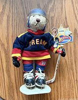 Front view of plush hockey bear on stand showing uniform, stick, tag and skates