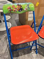Full view of one chair showing blue frame, orange seat, green backrest with Paw Patrol graphic