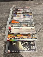 Stack of nine PS3 game cases showing titles on spines