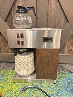 Front view coffee maker with carafe and taped plug visible