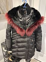 Front view of black Nicole Benisti parka hanging, showing red and black fur hood trim and quilting