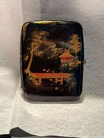 Front of black damascene cigarette case showing landscape design and clasp