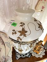 Lamp showing opaline glass body, brass floral decoration, crystal prisms and metal base