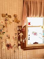 Wide shot of wall next to window showing numerous hanging angel ornaments of various materials and sizes