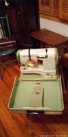 Elna Supermatic sewing machine set in open green metal case on floor