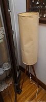 Full view of floor lamp with cylinder shade and tripod wood legs