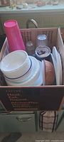 Box showing stacked Corelle plates/bowls, pink plastic tumbler, wooden bowl, travel mug, large plates