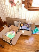 Two cardboard boxes containing wicker basket with note pads, teal organizer bin, various loose supplies