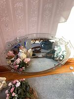 Front of oval mirror showing etched floral border, beveled edge, and scalloped outline