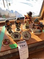 Four Hummel figurines and three small floral dishes on shelf