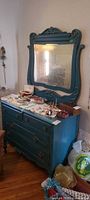 Front view showing dresser, attached ornate mirror, teal distressed finish, four drawers, brass pulls