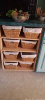 Six wicker baskets in cabinet cubbies with liners; glass bowl of faux fruit sitting on countertop