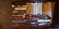 Box containing approximately 50 books, mix of paperback classics, fantasy series, biography and few hardcovers; visible titles noted