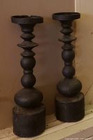 Two tall dark candlesticks leaning against wall