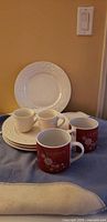 Stack of white embossed plates with two white mugs and two red Godiva mugs