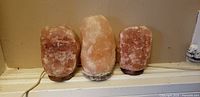 Front view of three Himalayan salt lamps showing crystal color, bases and cords