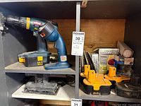 Ryobi drill on shelf with attached 18V battery; Black & Decker finishing sander beneath; three Ryobi yellow/black 18V batteries and packaged accessories visible