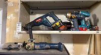 Top shelf showing Ryobi reciprocating saw, Ryobi drill (chuck missing), Makita drill with red battery