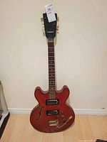 Full view of red Framus semi-hollow electric guitar standing against wall