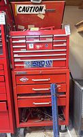 Full front view of red Mastercraft tool chest with drawers, blue clamps leaning against base, open lower compartment showing loose items