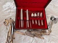 Open wooden chest with red lining showing organized flatware and surrounding loose pieces
