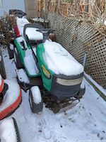 Front left view of green Weed Eater riding mower covered in snow beside red equipment