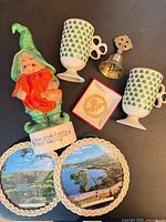 All items grouped: leprechaun bottle, two shamrock mugs, brass cross bell, Claddagh ornament, two scenic plaques