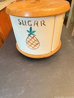 Side view showing sugar panel with pineapple graphic and wood lid