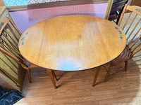 Top view of oval drop-leaf table between two matching chairs, showing stencil decoration and wood finish