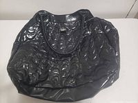 Full view of glossy black quilted duffle purse