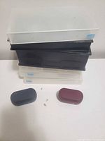 Stack of five VHS storage cases with two closed earbud charging cases in foreground