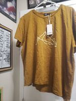 Front view of mustard yellow women’s T-shirt with mountain graphic and tag