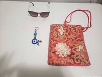 All three items laid out: sunglasses, brocade pouch, evil eye keychain