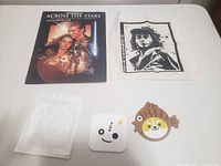Front view showing sheet music booklet, printed cloth, empty plastic bag, white coaster, fish coaster