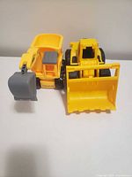 Two yellow plastic toy construction vehicles, CAT front loader and generic excavator-dump truck, front view