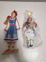 Front view of both dolls, one on stand, one packaged