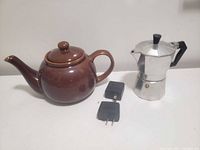 Side view of ceramic teapot, moka pot, and two USB chargers