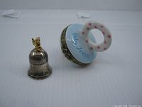 Both baby tooth holders side by side: Birks silver-plated bell with angel and ceramic pacifier holder open