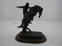 Left side view of bronze-tone cowboy on rearing horse figurine showing overall form and wooden base