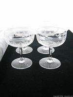 Four of the six matching etched crystal champagne coupes on black background