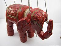 Front-side view of red wooden elephant marionette showing strings and paint details