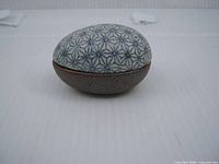 Side view of ceramic egg trinket dish showing blue geometric pattern and brown base