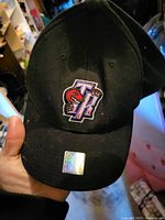 Front view of black cap showing embroidered TR raptor logo and brim sticker; visible lint indicating use