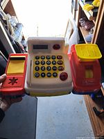 Front view of plastic toy cash register showing keypad, cash drawer, scanner pad and scale platform