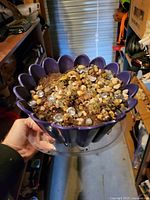 Hand-held view of purple scalloped planter containing succulents, gravel, glass stones, and clear saucer