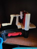 Side view of plastic and metal hand-crank apple peeler, corer and slicer on countertop base