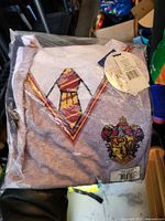 Front view of sealed Harry Potter Gryffindor T-shirt showing tie graphic, crest, and retail tag