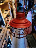 Matte red metal pendant lantern showing domed cap, cylindrical neck, wire cage, and hanging strap